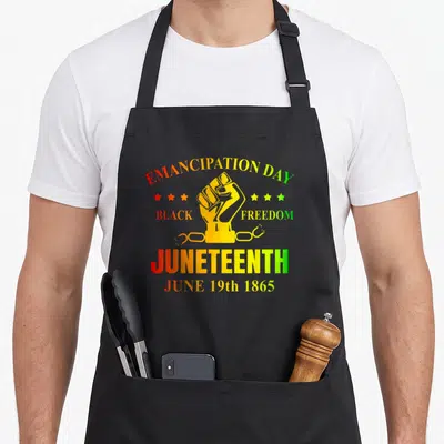 Juneteenth june african american aprons - Raised fist graphic with Emancipation Day text and broken chain in red orange — shown on a black cotton canvas apron against a white background
