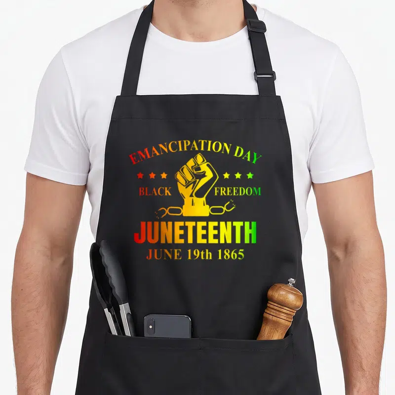 Juneteenth june african american aprons - Raised fist graphic with Emancipation Day text and broken chain in red orange — shown on a black cotton canvas apron against a white background
