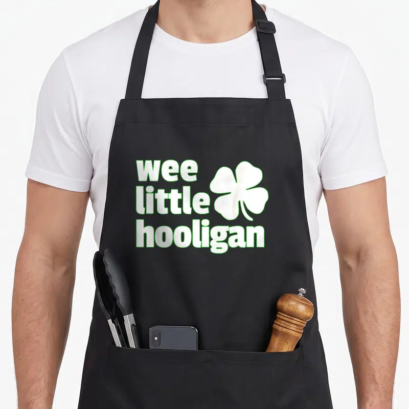Hooligan st patrick day aprons - Wee little hooligan text stacked beside shamrock in white with green outline — shown on a black cotton canvas apron against a white background