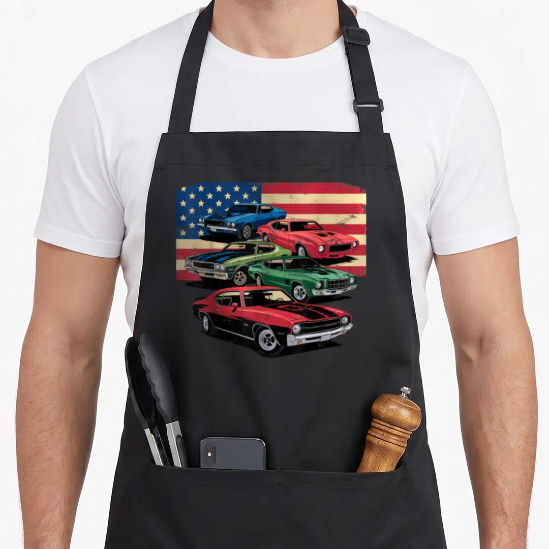 Patriotic muscle apron - Four muscle cars on distressed flag background in red white blue and green — shown on a black cotton canvas apron against a white background