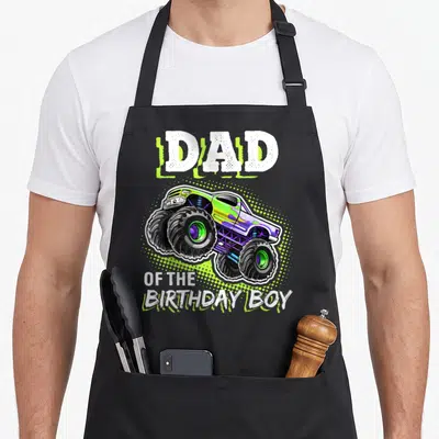 Vintage birthday truck apron - Dad of the Birthday Boy text above and below a lime green monster truck with purple — shown on a black cotton canvas apron against a white background