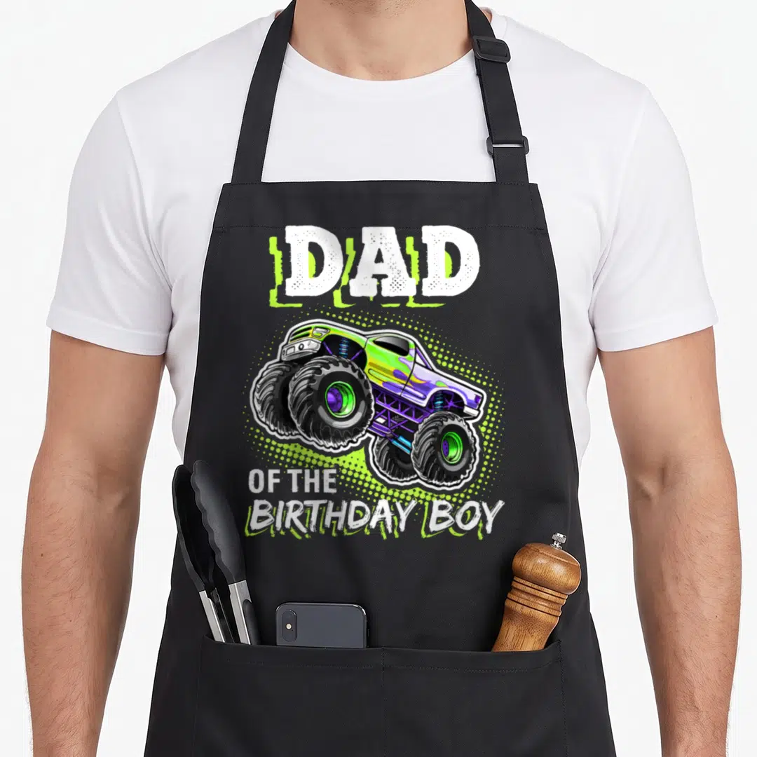 Vintage birthday truck apron - Dad of the Birthday Boy text above and below a lime green monster truck with purple — shown on a black cotton canvas apron against a white background