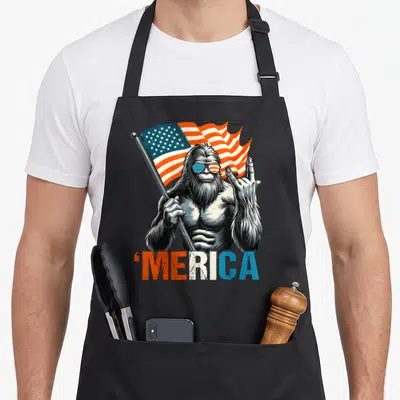 Rock 4th of july apron - Bigfoot holding flagpole with 'merica text in red white blue distressed style — shown on a black cotton canvas apron against a white background