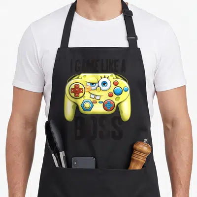 Squarepant boss apron - I GAME LIKE A BOSS text around yellow game controller with blue eyes and buck teeth — shown on a black cotton canvas apron against a white background