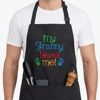 Grandchild granny apron - My Granny Loves Me text with red heart and green blue handprints — shown on a black cotton canvas apron against a white background