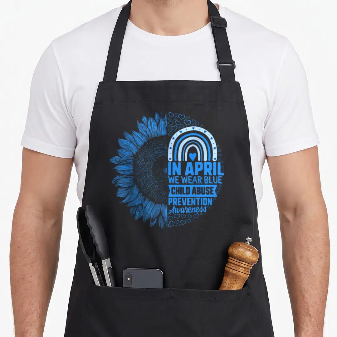 Abuse prevention april apron - Blue split sunflower with rainbow hearts and text In April We Wear Blue Child Abuse — shown on a black cotton canvas apron against a white background