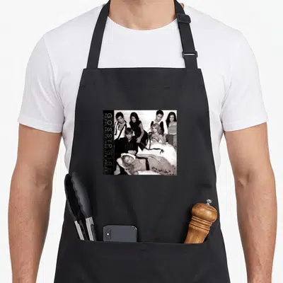 Retro gossip apron - Six people in formal wear next to vertical text reading Gossip Girl popularity has its price — shown on a black cotton canvas apron against a white background