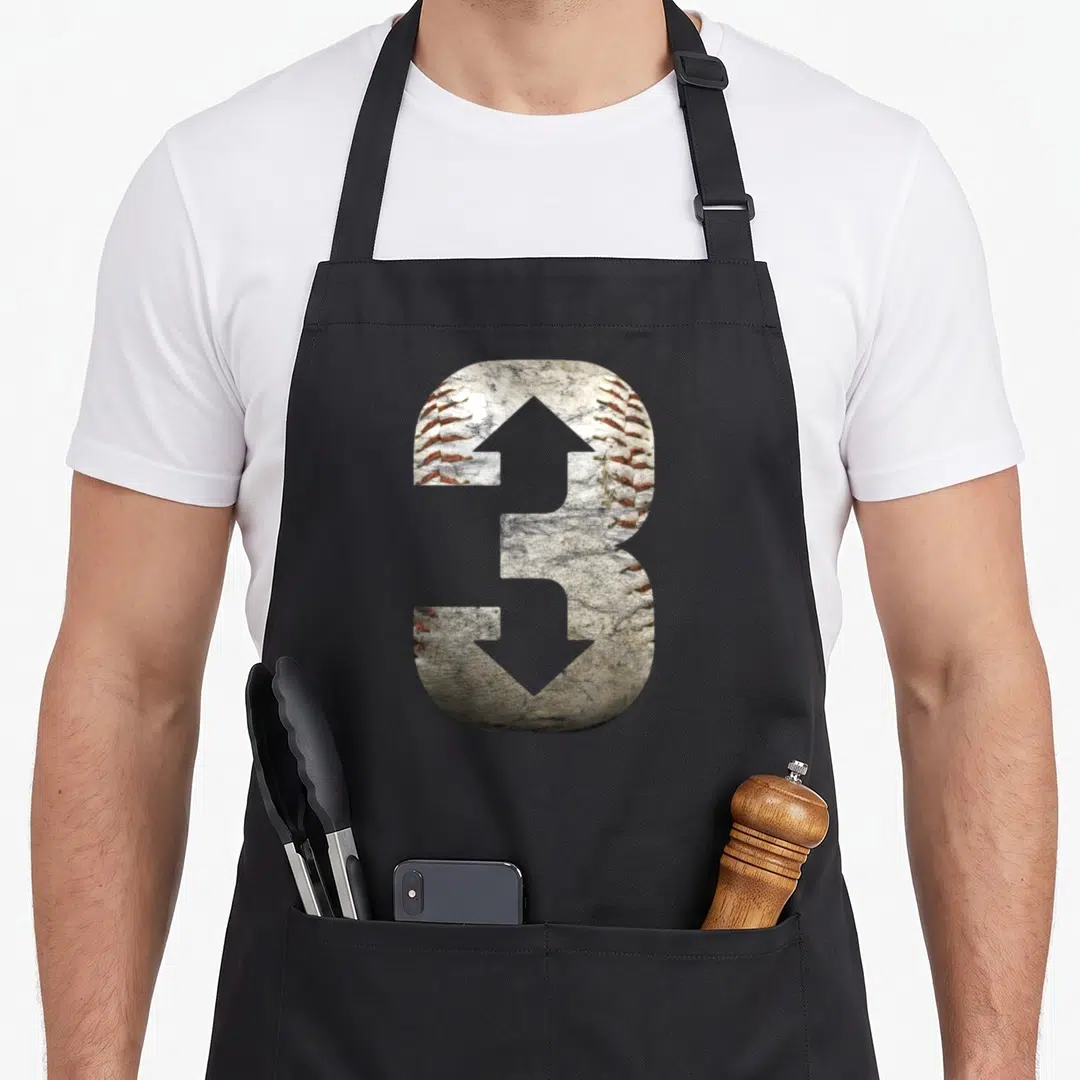 Three baseball apron - Number 3 filled with baseball leather texture and red stitching — shown on a black cotton canvas apron against a white background