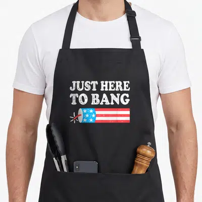 Bang 4th of july apron - Just Here To Bang text above horizontal red white blue firework with lit fuse — shown on a black cotton canvas apron against a white background