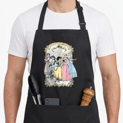 Once princess apron - Five princesses in gold frame with crown and pink blue yellow dresses — shown on a black cotton canvas apron against a white background