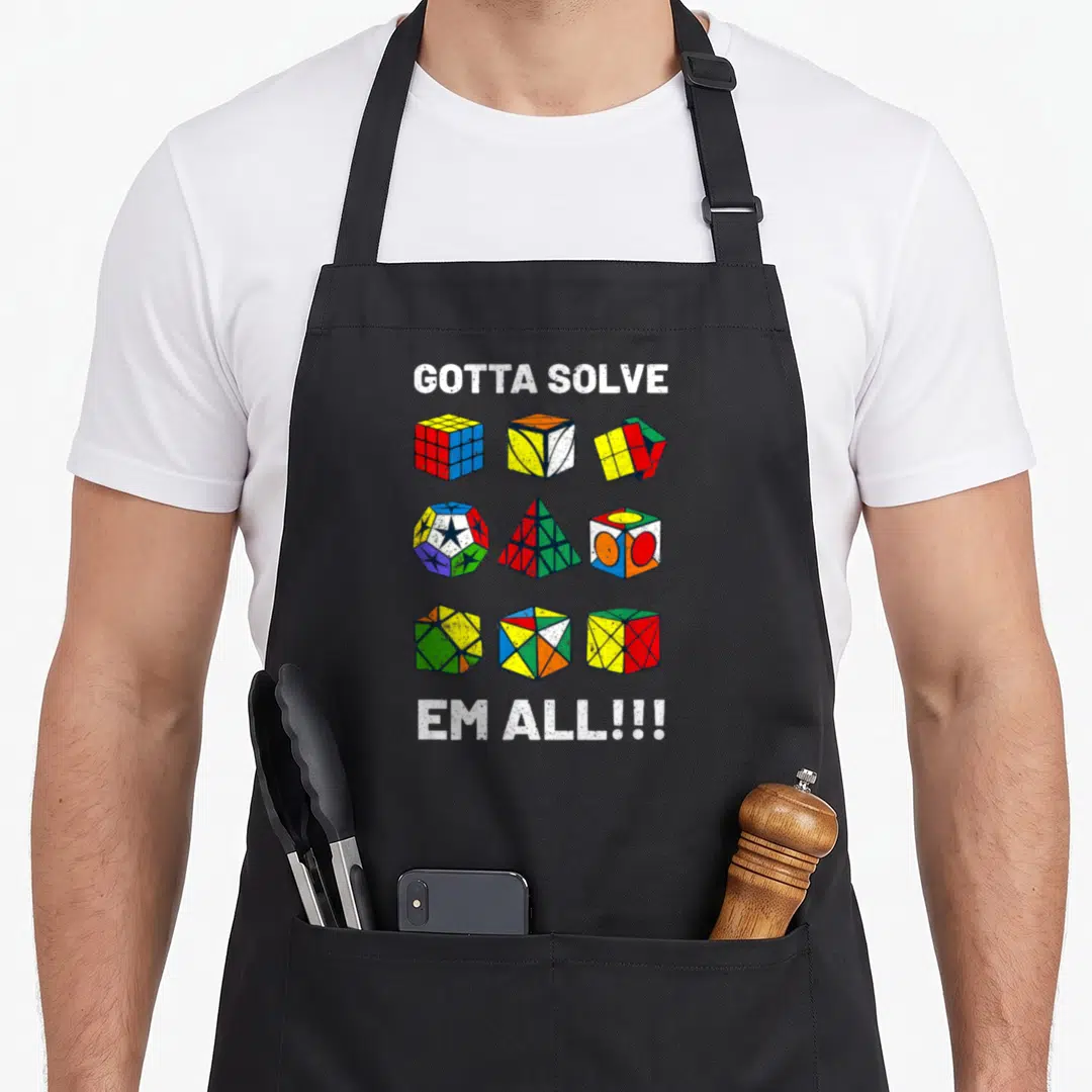Competitive speed girl apron - Nine colorful puzzle cubes in a grid with GOTTA SOLVE EM ALL text — shown on a black cotton canvas apron against a white background