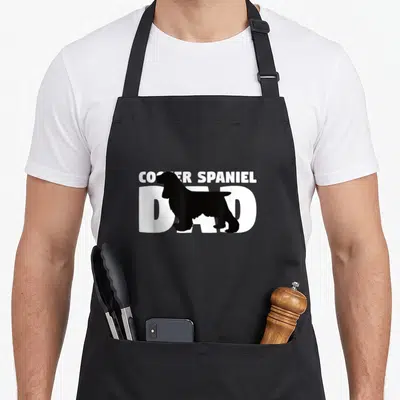 Father cocker spaniel apron - Black dog silhouette over white COCKER SPANIEL DAD text — shown on a black cotton canvas apron against a white background