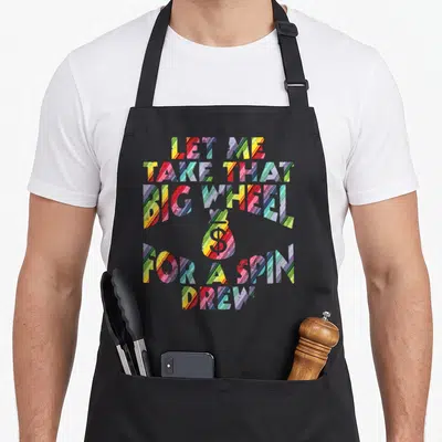 Spin wheel apron - Multicolored striped text reading LET ME TAKE THAT BIG WHEEL FOR A SPIN DREW with central money bag — shown on a black cotton canvas apron against a white background