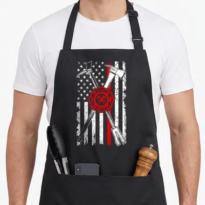 Patriotic firefighter apron - Distressed flag with crossed axes and red Maltese cross bearing FIRE DEPT. text — shown on a black cotton canvas apron against a white background