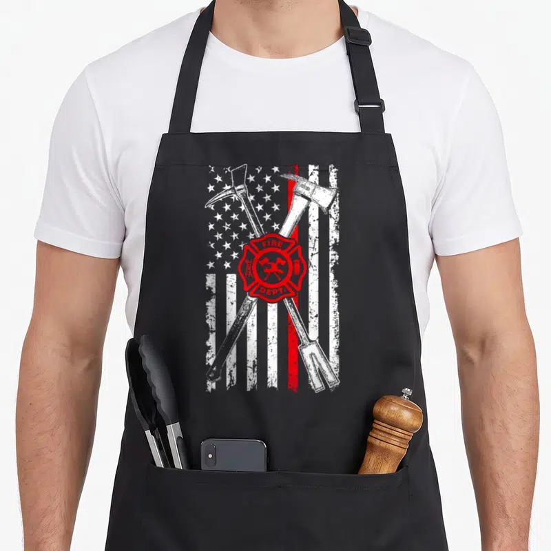 Patriotic firefighter apron - Distressed flag with crossed axes and red Maltese cross bearing FIRE DEPT. text — shown on a black cotton canvas apron against a white background