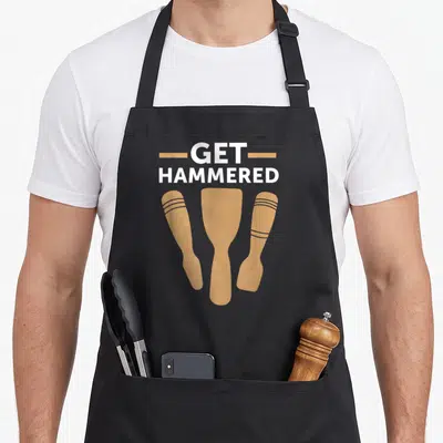 Hammered massage aprons - White GET HAMMERED text above three tan wooden hammer silhouettes — shown on a black cotton canvas apron against a white background