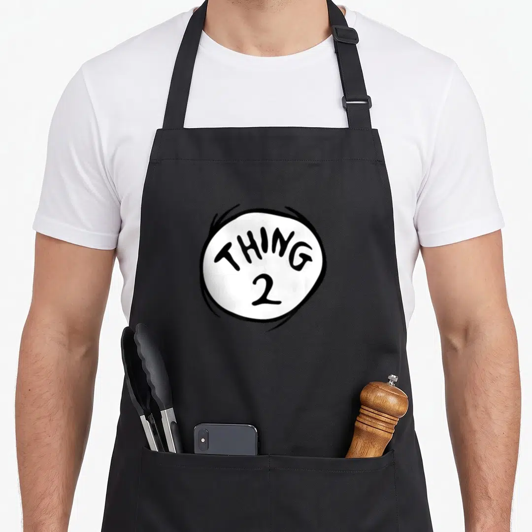 Funny emblem general apron - White circle with black THING 2 text and surrounding scribbles — shown on a black cotton canvas apron against a white background