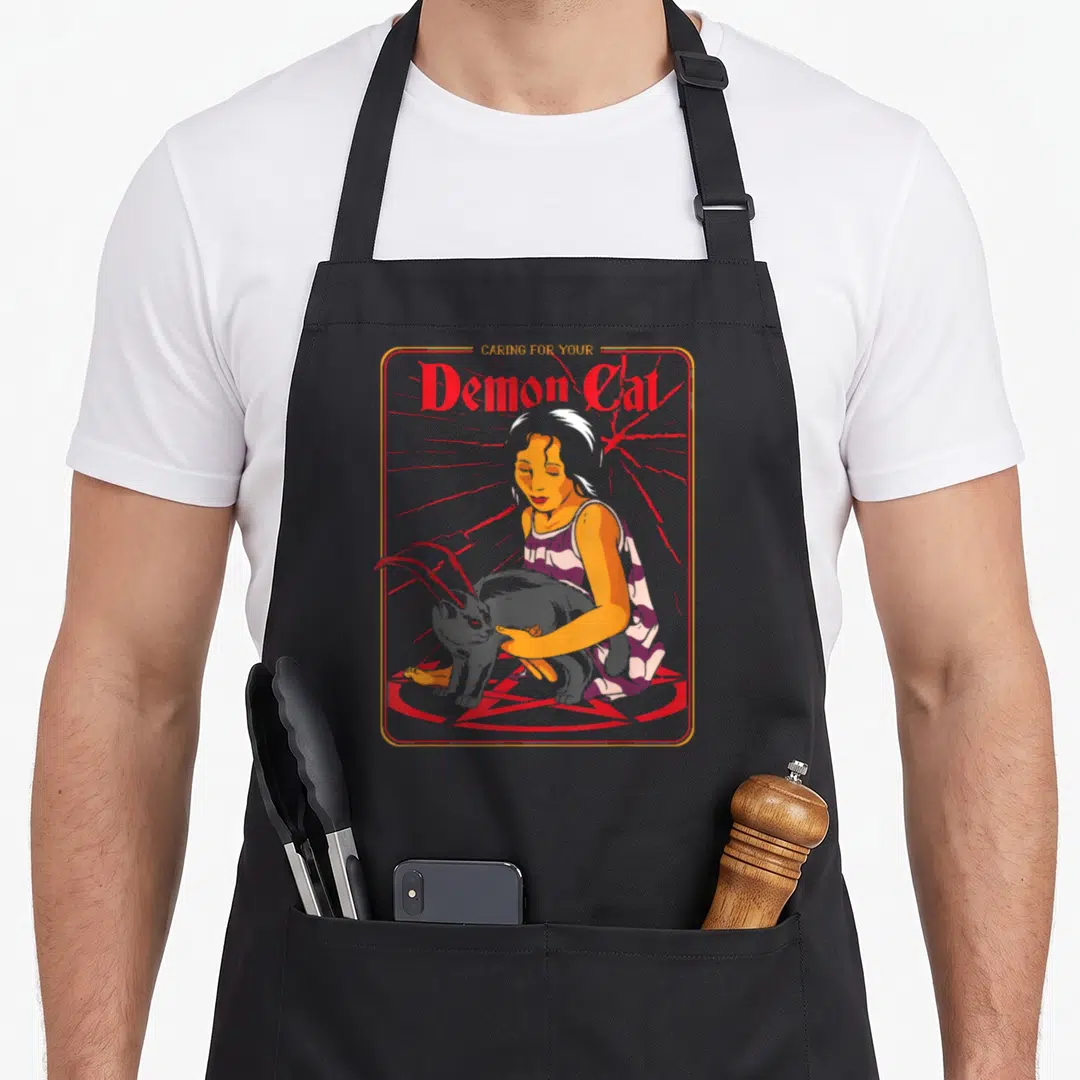 Caring funny cat aprons - Girl holding horned cat on red pentagram with stacked text — shown on a black cotton canvas apron against a white background