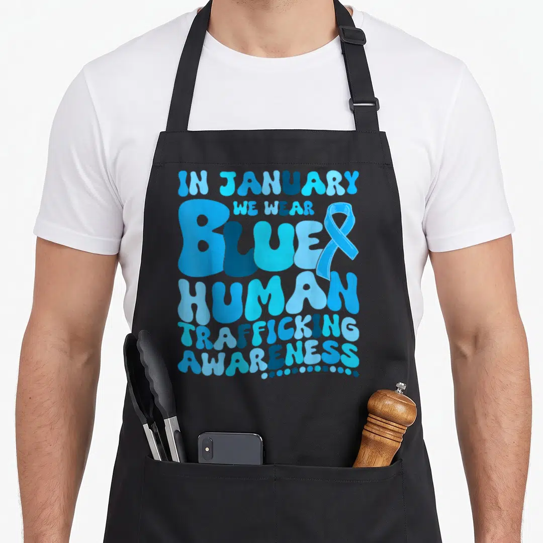 Human trafficking ribbon apron - Stacked blue bubble text reading In January We Wear Blue Human Trafficking Awareness — shown on a black cotton canvas apron against a white background