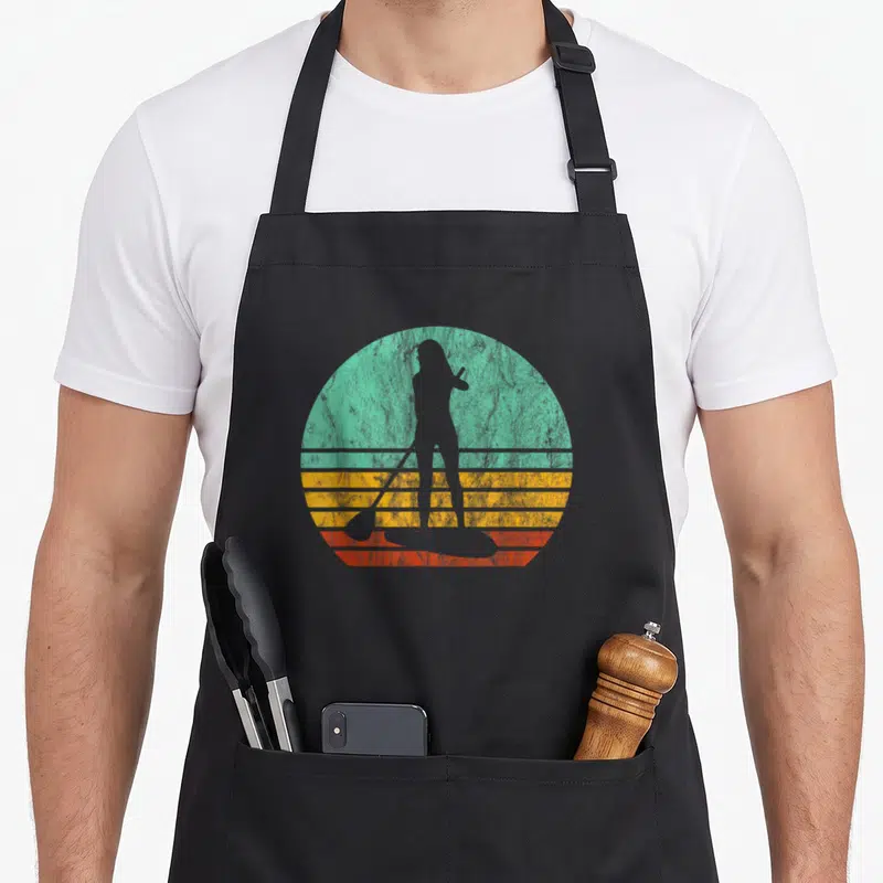 Sup stand paddleboard apron - Retro grey woman silhouette on paddleboard against teal yellow orange striped circle — shown on a black cotton canvas apron against a white background
