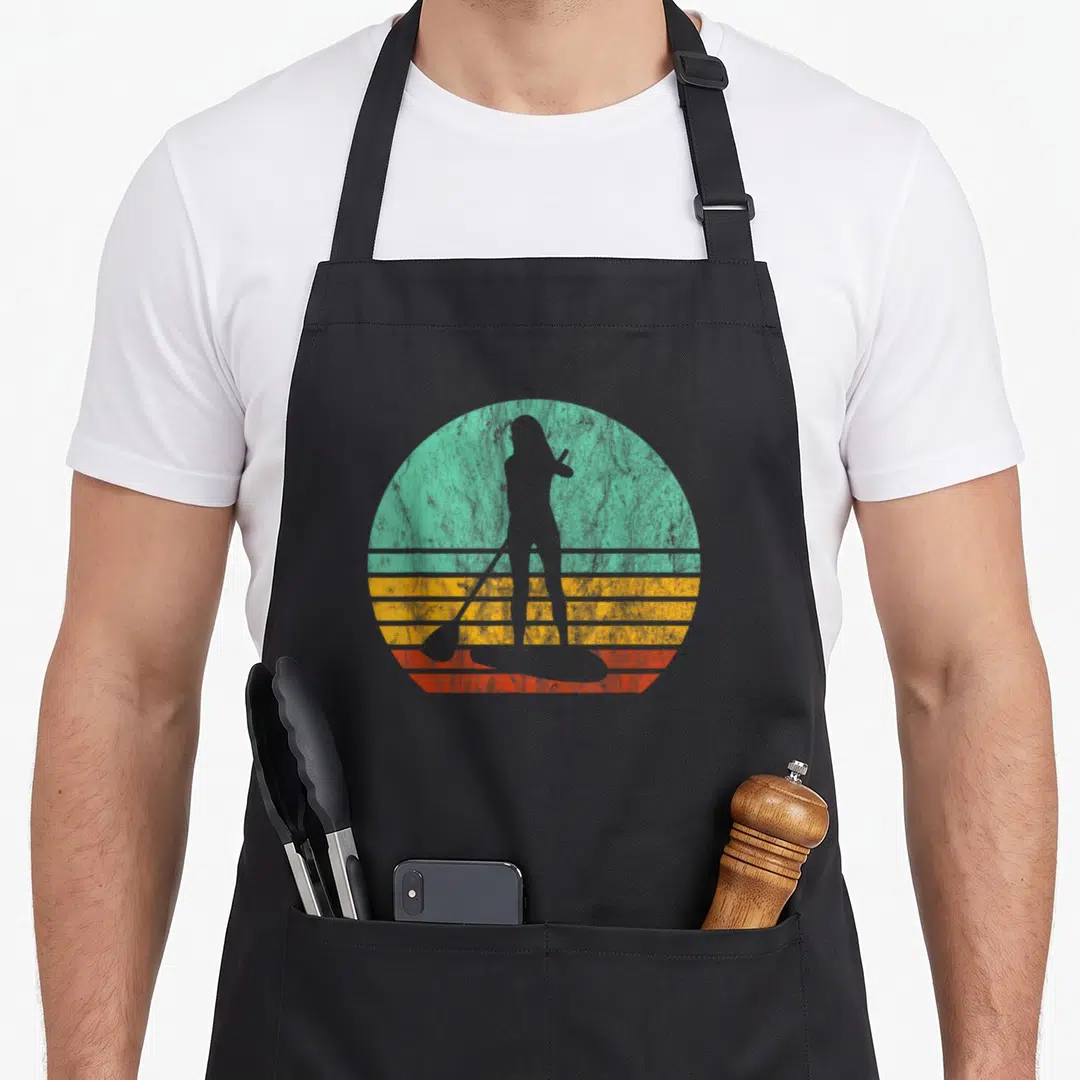 Sup stand paddleboard apron - Retro grey woman silhouette on paddleboard against teal yellow orange striped circle — shown on a black cotton canvas apron against a white background