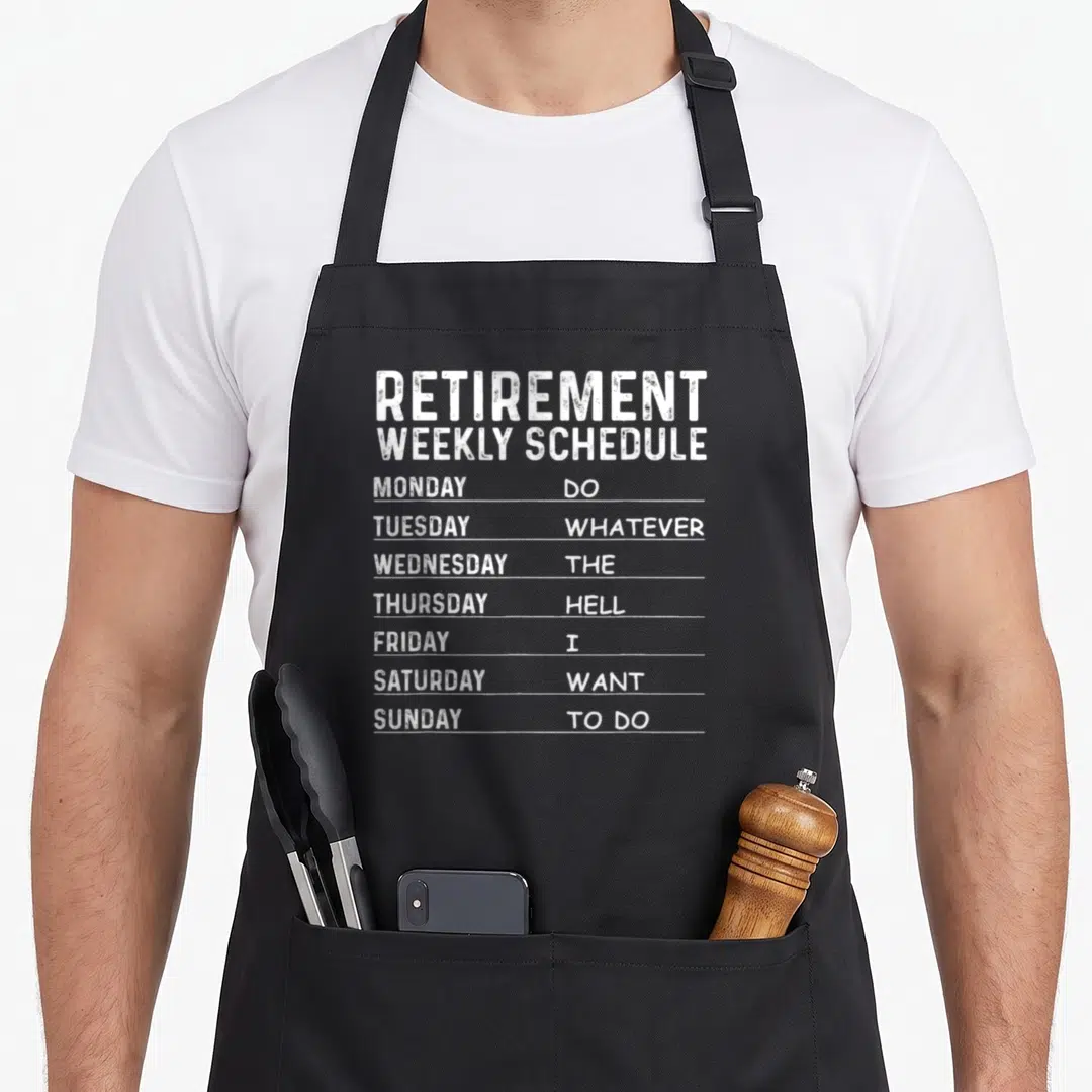 Retiree retirement apron - White text reading Retirement Weekly Schedule listing days from Monday to Sunday — shown on a black cotton canvas apron against a white background