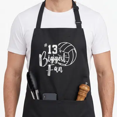 Thirteen volleyball dad apron - White line art volleyball and #13 is Biggest Fan text on black apron — shown on a black cotton canvas apron against a white background