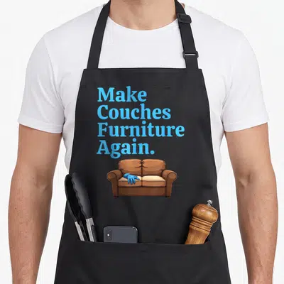 Couch king apron - Make Couches Furniture Again text above brown cartoon couch with blue glove — shown on a black cotton canvas apron against a white background