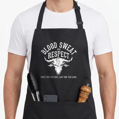 Die blood apron - White distressed bull head with arched text BLOOD SWEAT AND RESPECT above and bottom caption — shown on a black cotton canvas apron against a white background