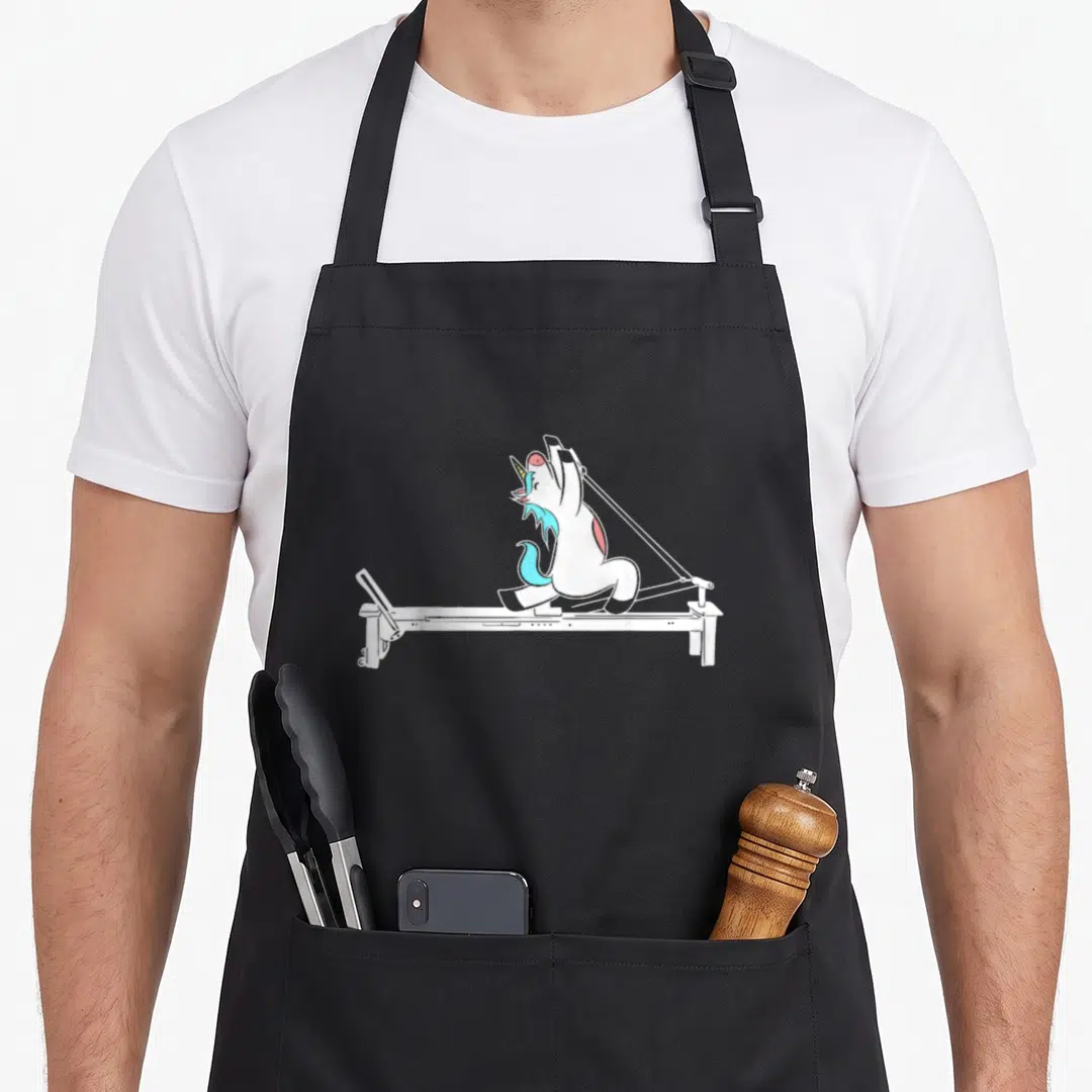 Pilate training apron - Cartoon white unicorn with cyan mane pulling reformer straps upwards — shown on a black cotton canvas apron against a white background