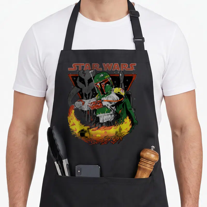 Poster flame apron - Boba Fett in green armor with STAR WARS text above a fiery landscape — shown on a black cotton canvas apron against a white background