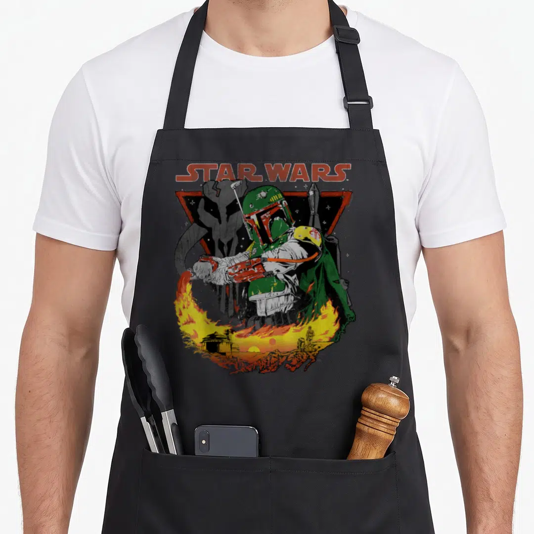 Poster flame apron - Boba Fett in green armor with STAR WARS text above a fiery landscape — shown on a black cotton canvas apron against a white background