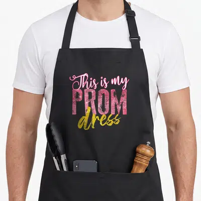 Dress funny prom apron - Stacked pink and yellow text reading This is my PROM dress — shown on a black cotton canvas apron against a white background