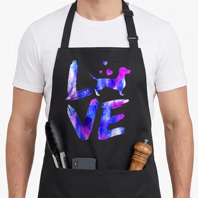 Daschund doxie dog apron - Watercolor purple and blue dog replacing letter O in LOVE with three floating hearts — shown on a black cotton canvas apron against a white background
