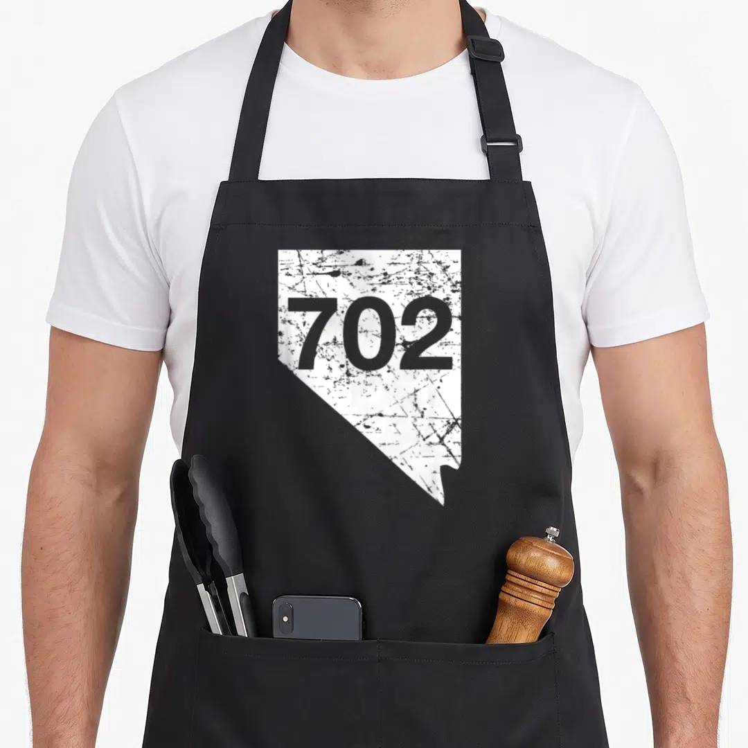 Henderson nevada girl apron - White distressed Nevada state outline containing the grey number 702 in the center — shown on a black cotton canvas apron against a white background