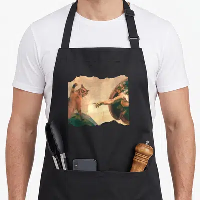 Swatting cat apron - Orange cat facing outstretched hand on torn beige paper background — shown on a black cotton canvas apron against a white background