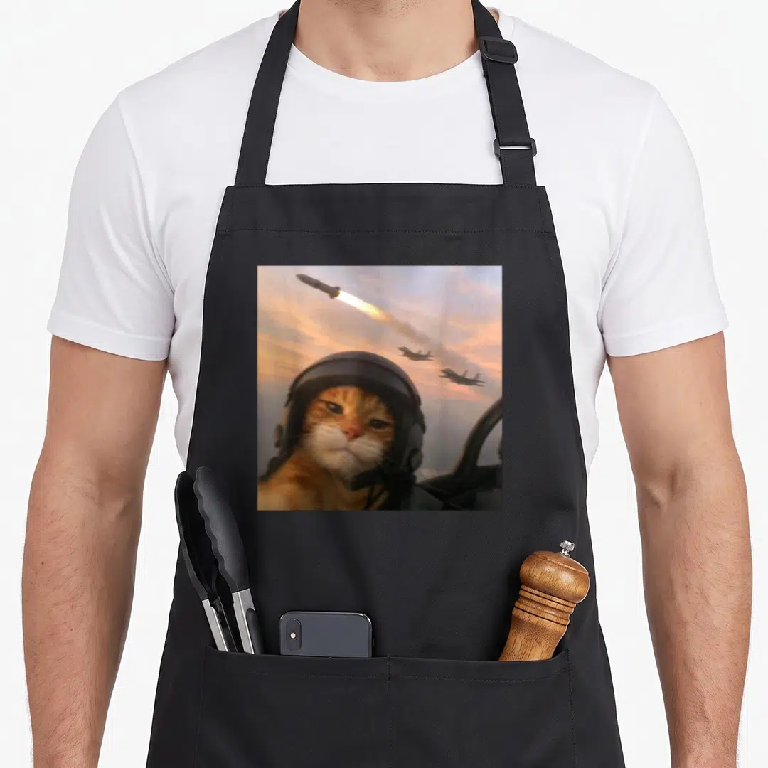 Selfie kitty cat apron - Orange cat in pilot helmet with missile and two jets flying in sky — shown on a black cotton canvas apron against a white background