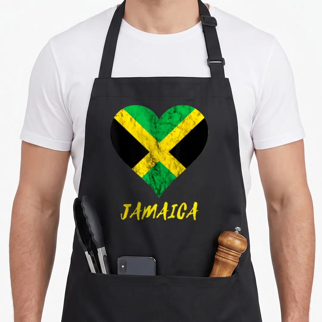 Jamaica travel aprons - Distressed heart with green yellow black flag pattern above yellow JAMAICA text — shown on a black cotton canvas apron against a white background