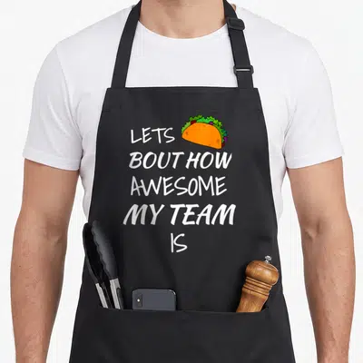 Appreciation boss employee aprons - Stacked white text reading LETS BOUT HOW AWESOME MY TEAM IS next to an orange — shown on a black cotton canvas apron against a white background