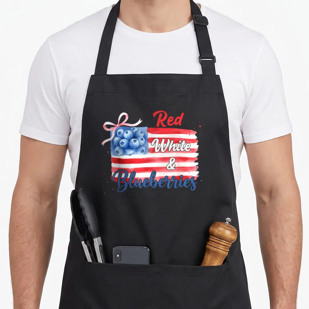 Cute blueberries apron - Watercolor USA flag with blueberry canton, pink ribbon, stacked red white & blueberries text — shown on a black cotton canvas apron against a white background