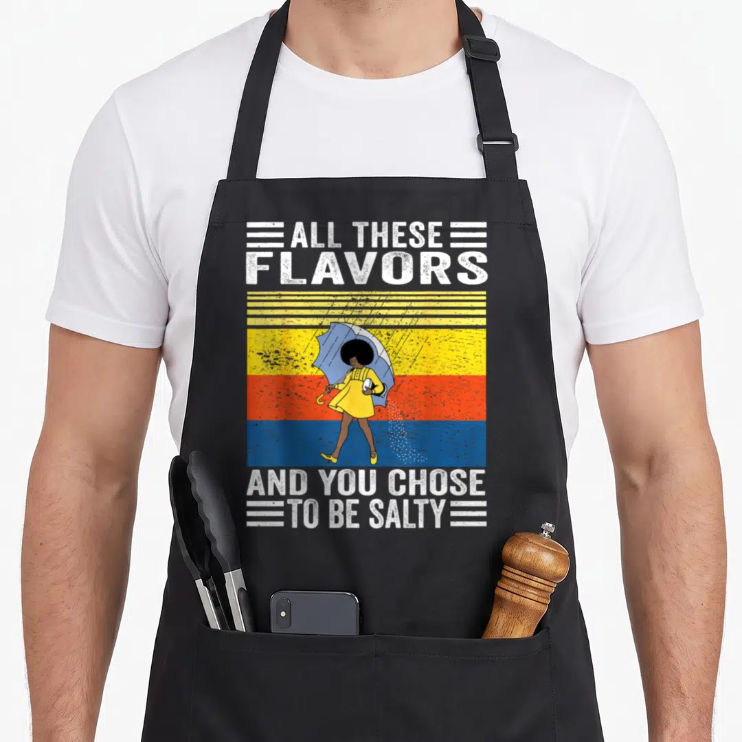 Chose these apron - Cartoon woman in yellow dress with blue umbrella against yellow orange blue stripes with white text — shown on a black cotton canvas apron against a white background