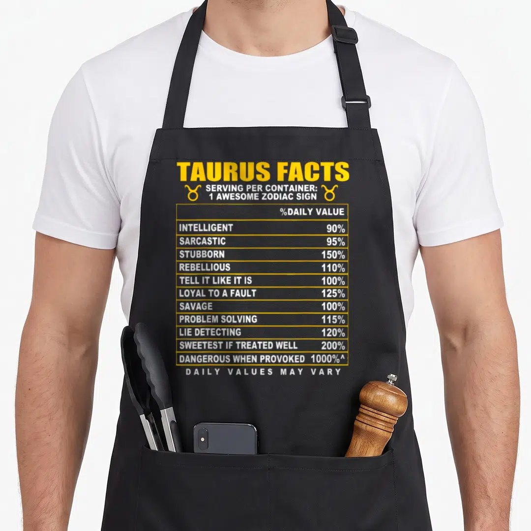 Funny fact taurus aprons - Yellow and white nutrition facts table listing Taurus traits like sarcastic and stubborn — shown on a black cotton canvas apron against a white background