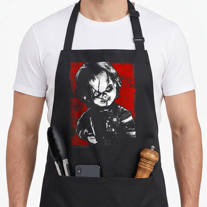 Play distressed apron - Grey and white doll holding knife on distressed red background — shown on a black cotton canvas apron against a white background