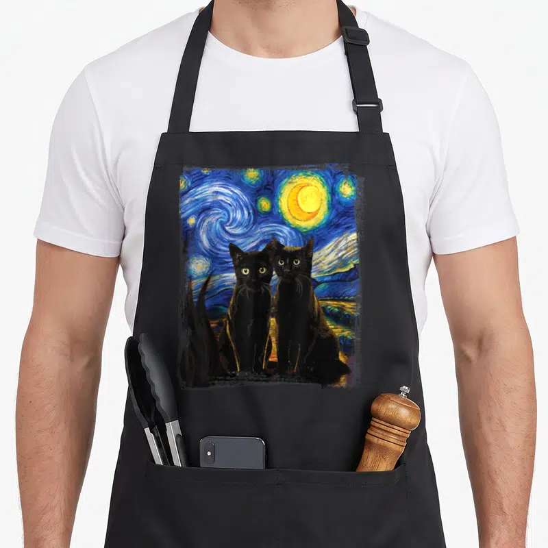 Painting van gogh apron - Two black cats sitting before a blue and yellow swirling starry night watercolor painting — shown on a black cotton canvas apron against a white background