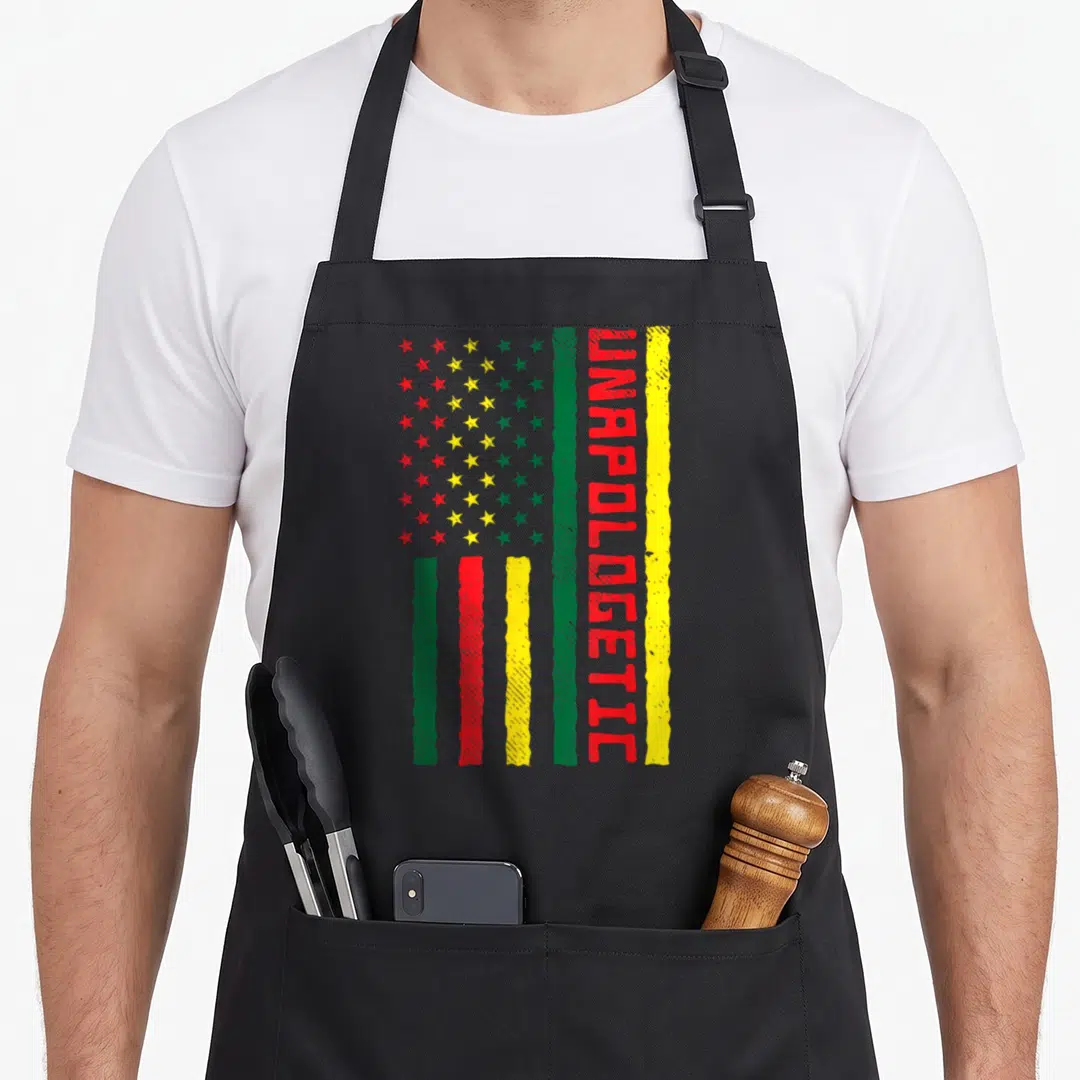 Unapologetic american flag apron - Distressed flag print with green red and yellow stars and vertical UNAPOLOGETIC text — shown on a black cotton canvas apron against a white background