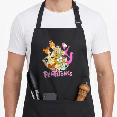 Shot family aprons - Flintstones cartoon characters in circle with pink title text — shown on a black cotton canvas apron against a white background