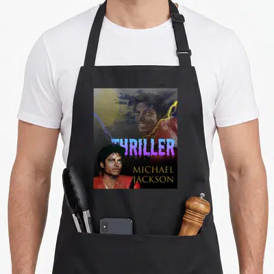 Performance michaels apron - Two Michael Jackson photos with purple THRILLER text and gold name on dark background — shown on a black cotton canvas apron against a white background