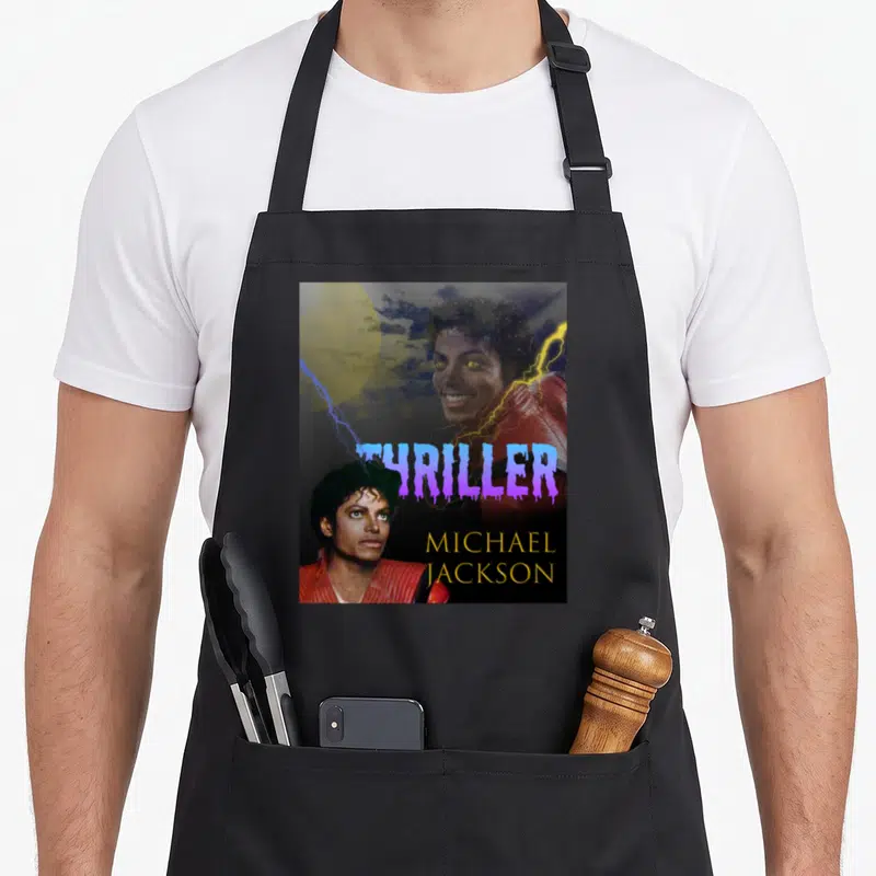 Performance michaels apron - Two Michael Jackson photos with purple THRILLER text and gold name on dark background — shown on a black cotton canvas apron against a white background