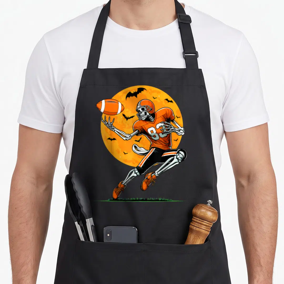Football skeleton player halloween apron - Leaping skeleton football player in orange jersey with number 83 and bats — shown on a black cotton canvas apron against a white background
