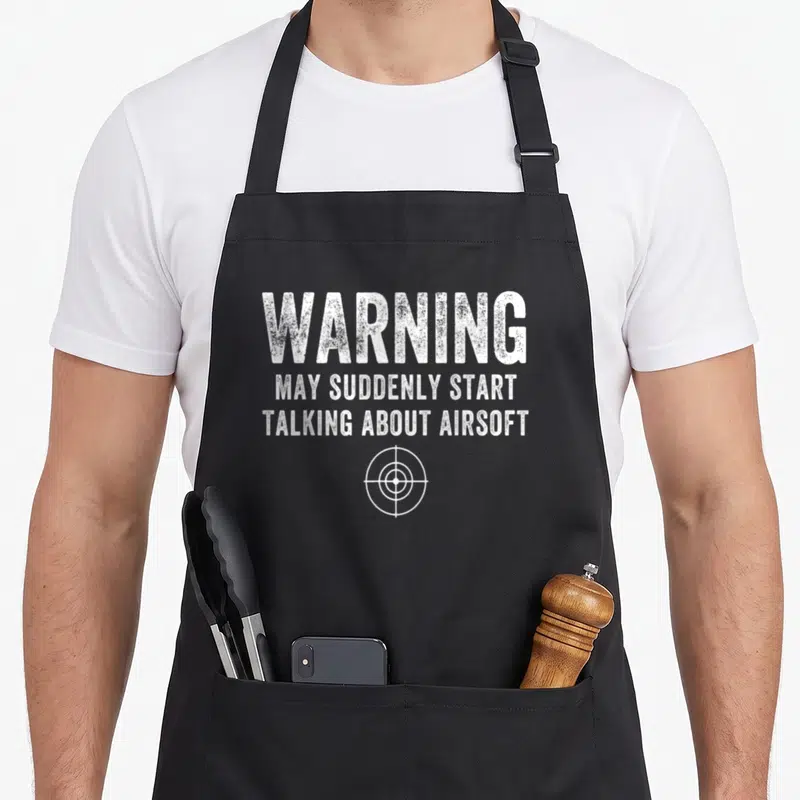 Airsoft outdoor apron - White distressed text WARNING MAY SUDDENLY START TALKING ABOUT AIRSOFT above target symbol — shown on a black cotton canvas apron against a white background
